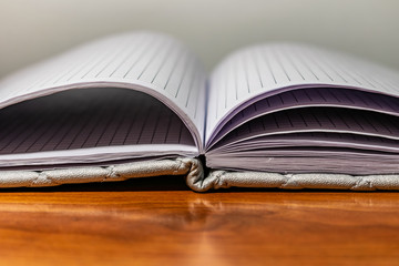 A book, a notebook with a checkered pattern on a wooden table in different poses. The cover is grey and soft with texture. Square patterns stitched with threads. Write notes in a diary. Plain white pa