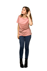 A full-length shot of a Teenager girl with pink sweater listening to something by putting hand on the ear on isolated white background