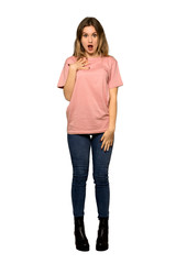 A full-length shot of a Teenager girl with pink sweater surprised and shocked while looking right on isolated white background