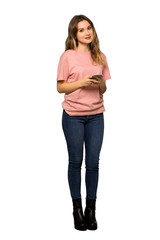 A full-length shot of a Teenager girl with pink sweater sending a message with the mobile on isolated white background