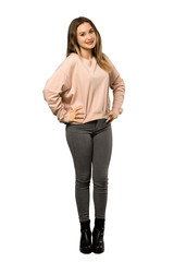A full-length shot of a Teenager girl with pink sweater posing with arms at hip and smiling over isolated white background