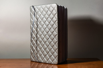 A book, a notebook with a checkered pattern on a wooden table in different poses. The cover is grey and soft with texture. Square patterns stitched with threads. Write notes in a diary. Plain white pa