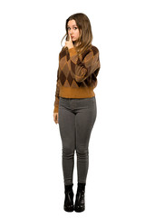 A full-length shot of a Teenager girl with brown sweater showing a sign of silence gesture putting finger in mouth over isolated white background