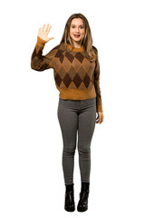 A full-length shot of a Teenager girl with brown sweater saluting with hand with happy expression over isolated white background