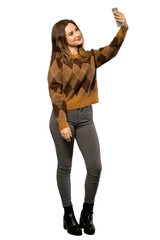 A full-length shot of a Teenager girl with brown sweater making a selfie over isolated white background