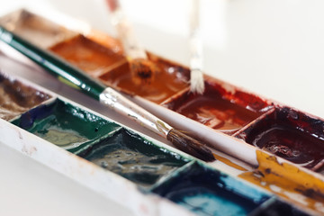 Several paint brushes and an old dirty watercolor palette with different natural colors