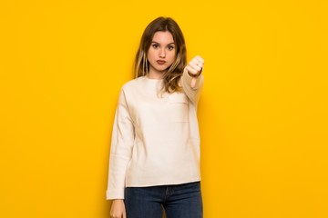 Teenager girl over yellow wall showing thumb down sign with negative expression