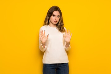 Fototapeta premium Teenager girl over yellow wall making stop gesture with both hands