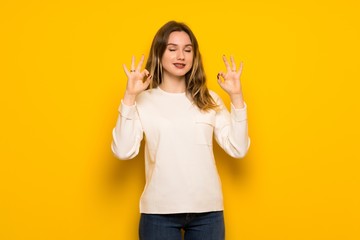 Teenager girl over yellow wall in zen pose