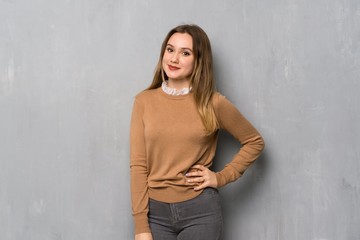 Teenager girl over textured wall posing with arms at hip and smiling