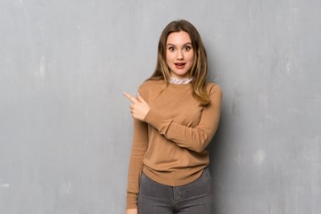 Teenager girl over textured wall surprised and pointing finger to the side