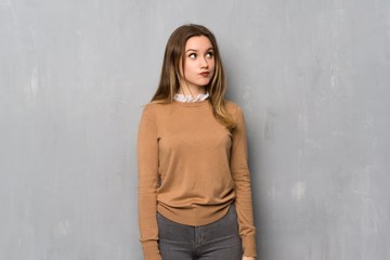 Teenager girl over textured wall with confuse face expression while bites lip