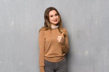 Teenager girl over textured wall giving a thumbs up gesture and smiling