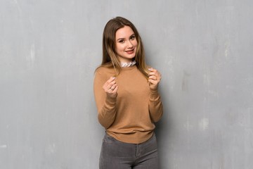 Teenager girl over textured wall making money gesture