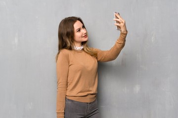 Teenager girl over textured wall making a selfie