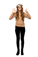 Obraz na płótnie Canvas Full-length shot of Young woman with beret showing ok sign with and giving a thumb up gesture on isolated white background