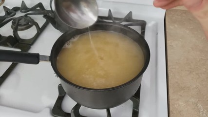 Home cooking -  Checking with ladle fresh made roasted Turkey broth or base in non-stick pot placed on the gas stove in preparation of making Ramen or soup.