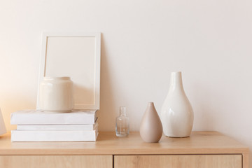 Neutral colored vases, photo frame and stack of books on bureau shelf