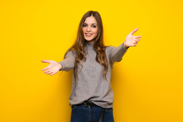 Young woman over yellow wall presenting and inviting to come with hand