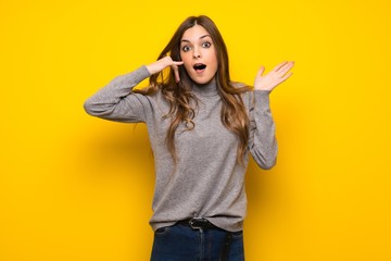 Young woman over yellow wall making phone gesture and doubting