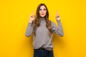 Young woman over yellow wall with fingers crossing and wishing the best