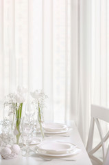 Happy Easter! Decor and table setting of the Easter table with white tulips and dishes of white color.