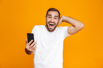 Photo of handsome man 30s in casual wear holding smartphone, isolated over yellow background