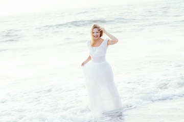 Fototapeta na wymiar Attractive happy mature tourist blonde woman in long white dress on asian sand tropical beach.