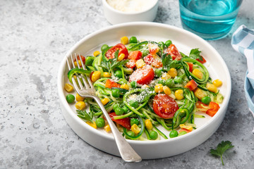 zucchini noodle with tomato, corn and green peas on white plate