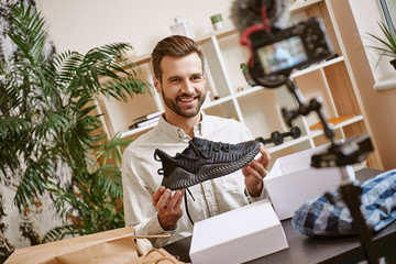 Sport shoes. Cheerful male blogger holding black sneakers while recording new video for his blog.