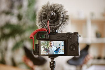 In focus. Close up photo of camera display with cheerful male blogger holding black sneakers while...