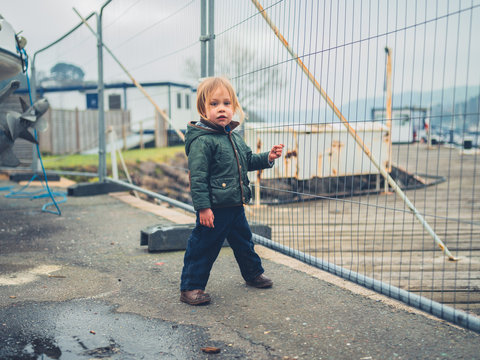 Little toddler standing by fence in boatyard