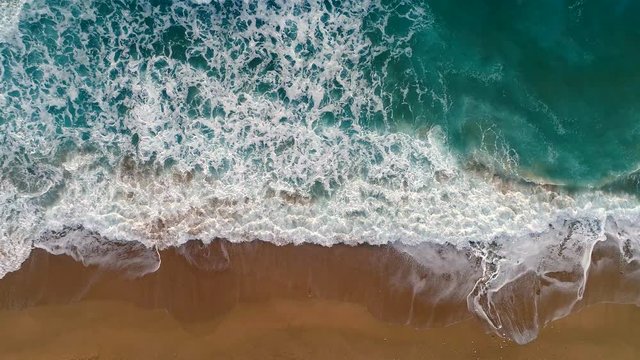 Sea or ocean surf wave. Foamy ocean waves rolling and coming on a sand beach. Aerial top down shot, 4K