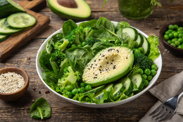 healthy vegan green salad with avocado, broccoli, cucumber, green peas and spinach in white  bowl