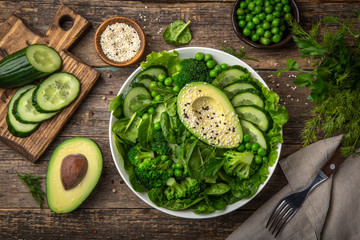 healthy vegan green salad with avocado, broccoli, cucumber, green peas and spinach in white  bowl