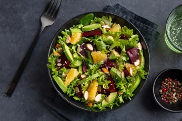 Poster healthy vegan avocado, orange and beet salad in black bowl, dark background © anna_shepulova