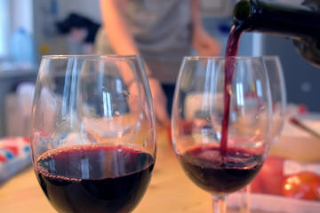Red wine is poured into wineglasses in the kitchen at home.