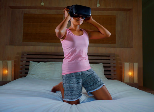 Fototapeta young attractive and happy woman on bed playing with VR virtual reality goggles video game having fun excited and surprised watching 3D illusion in digital entertainment