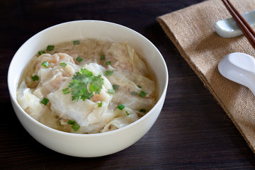 Shrimp wonton in hot soup in white bowl on dark wooden table, Asia food