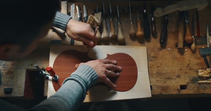 Slow motion close up of master artisan luthier working on creation of handmade violin  in a workshop. Shot in 8K. Concept of spiritual instrument, handmade, art, orchestra, artisan, passion for music