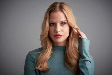 Fototapeta premium Portrait of blond young woman looking at camera and smiling while posing at light grey background