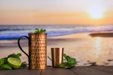 Cold Moscow Mules cocktail with ginger beer, vodka and lime over beach and seaside background