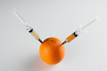 Orange injections on a black background on a wooden table, GMOs and nitrates