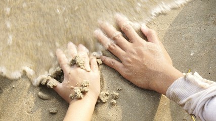 Image of two hands on sand of a beach with waves coming 