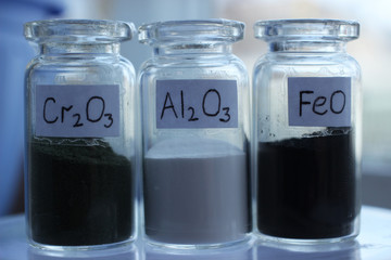 Metal oxides in glass jars: dark green chromium oxide, white aluminium oxide, black iron oxide.