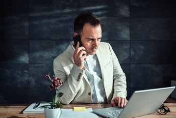 Businessman talking on smart phone and using laptop