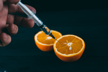 Orange injections on a black background on a wooden table, GMOs and nitrates
