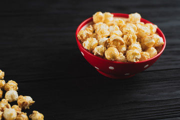 popcorn with caramel in a red plate on a black wooden background scattered