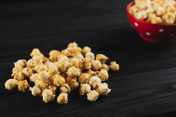 popcorn with caramel in a red plate on a black wooden background scattered