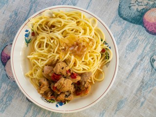 Top view on a plate with pasta and pieces of pork meat fried in vegetables